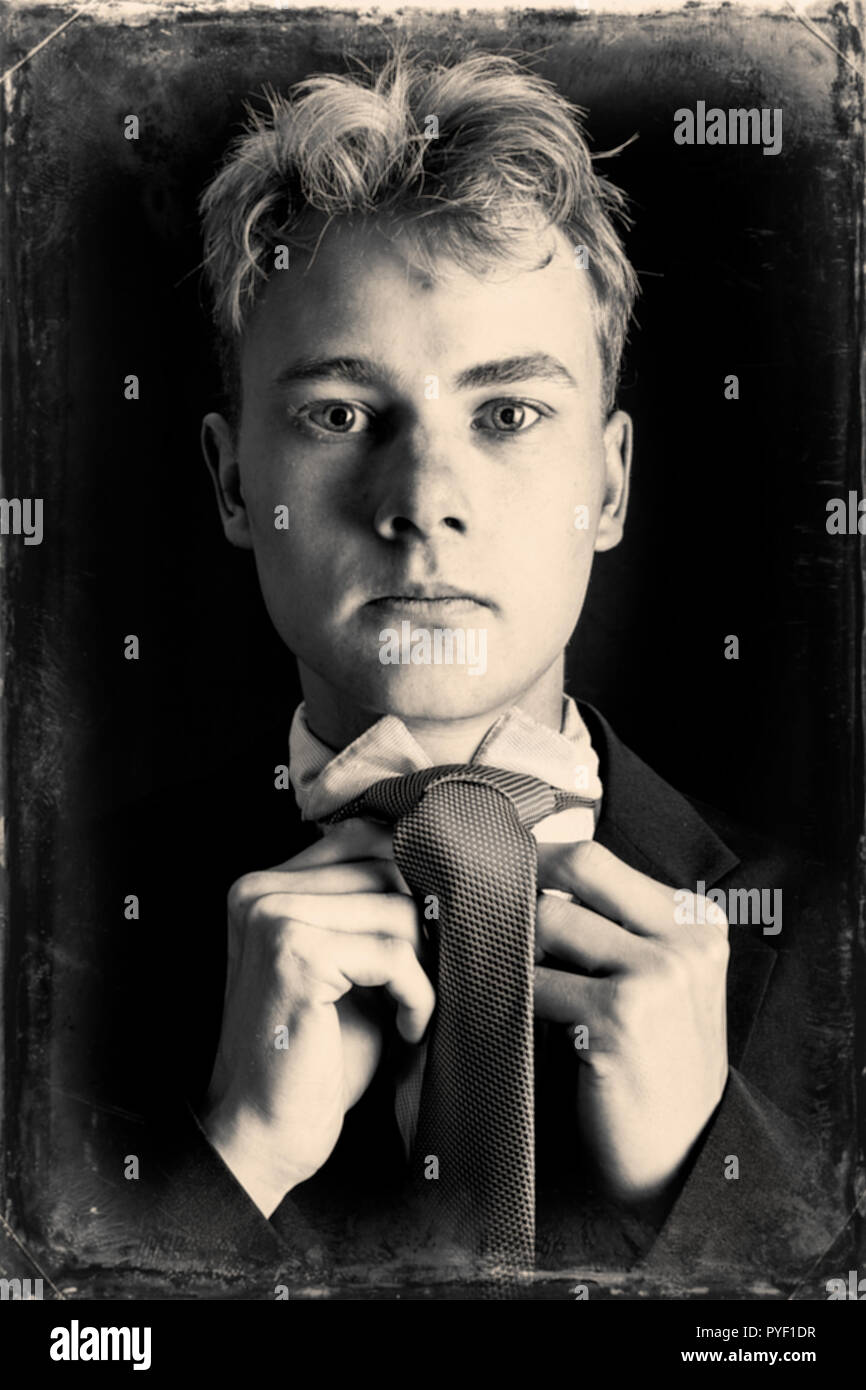 Young blonde caucasian adult male tying a tie finished in wet plate sepia for a vintage look Stock Photo