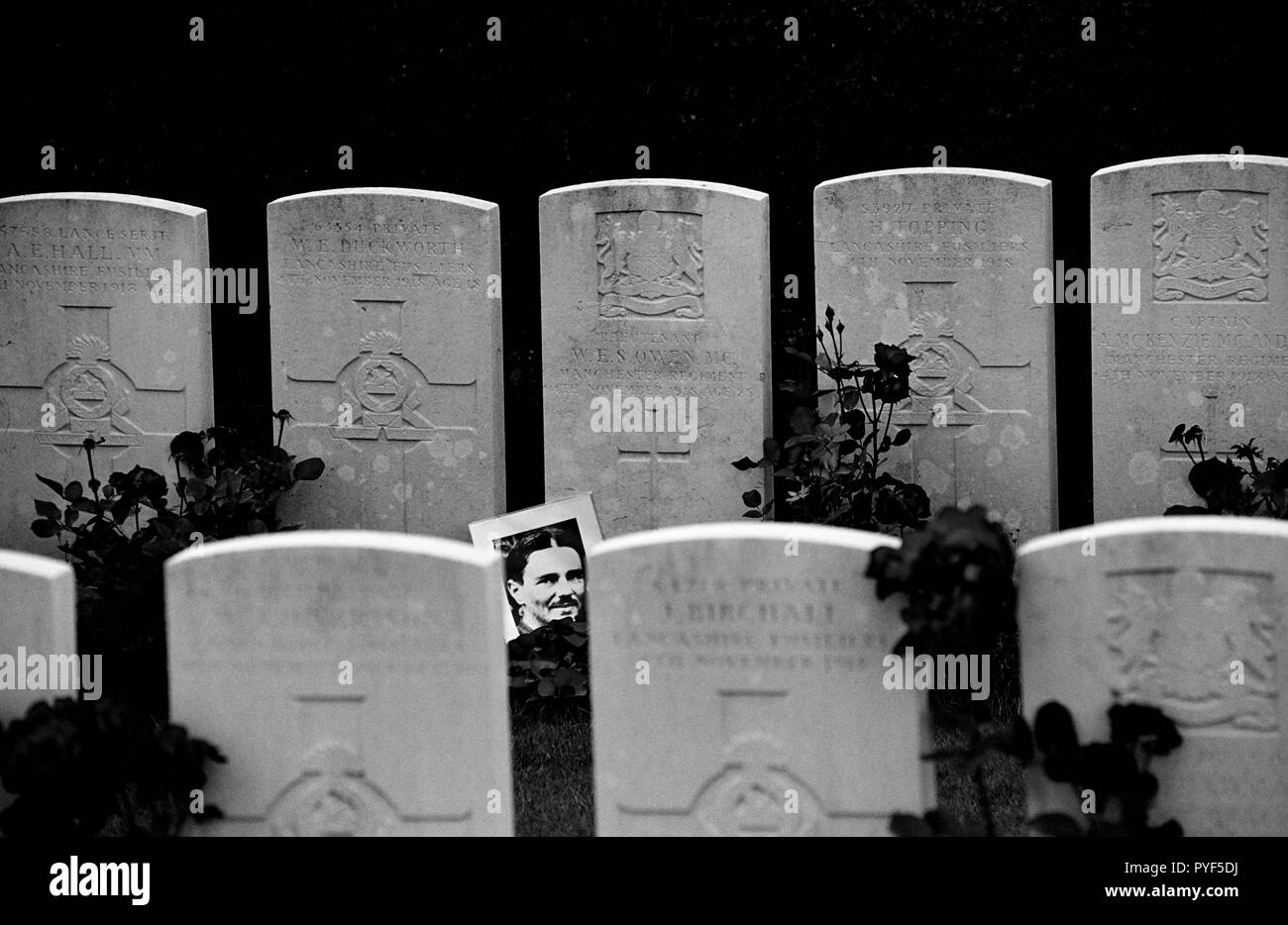 Wilfred Owen the poet died on 4th November 1918 just 7 days before the end of the first world war. A photograph of Owen normally rests against his grave at Ors Communal Cemetery  in the Commonwealth WarGraves Commission plot. The town of Ors is a commune in the Nord department in northern France can be seen in the background and the spot where Owen died is just behind the Church spire in the background of this photograph. Owen was killed in action on 4 November 1918 during the crossing of the Sambre–Oise Canal, exactly one week (almost to the hour) before the signing of the Armistice which end Stock Photo