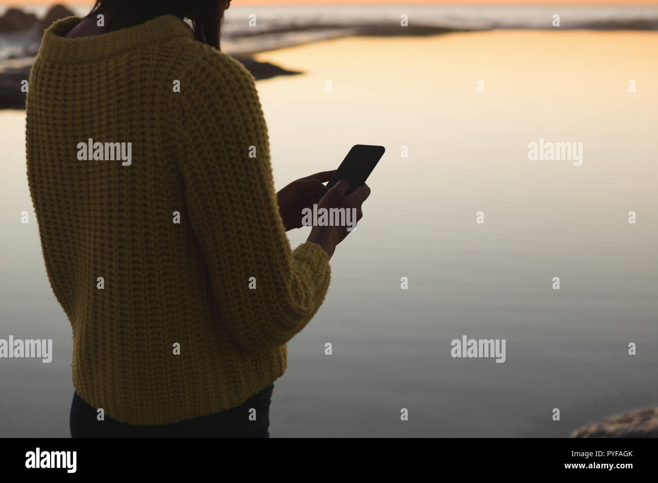 Woman using mobile phone on beach during sunset Stock Photo