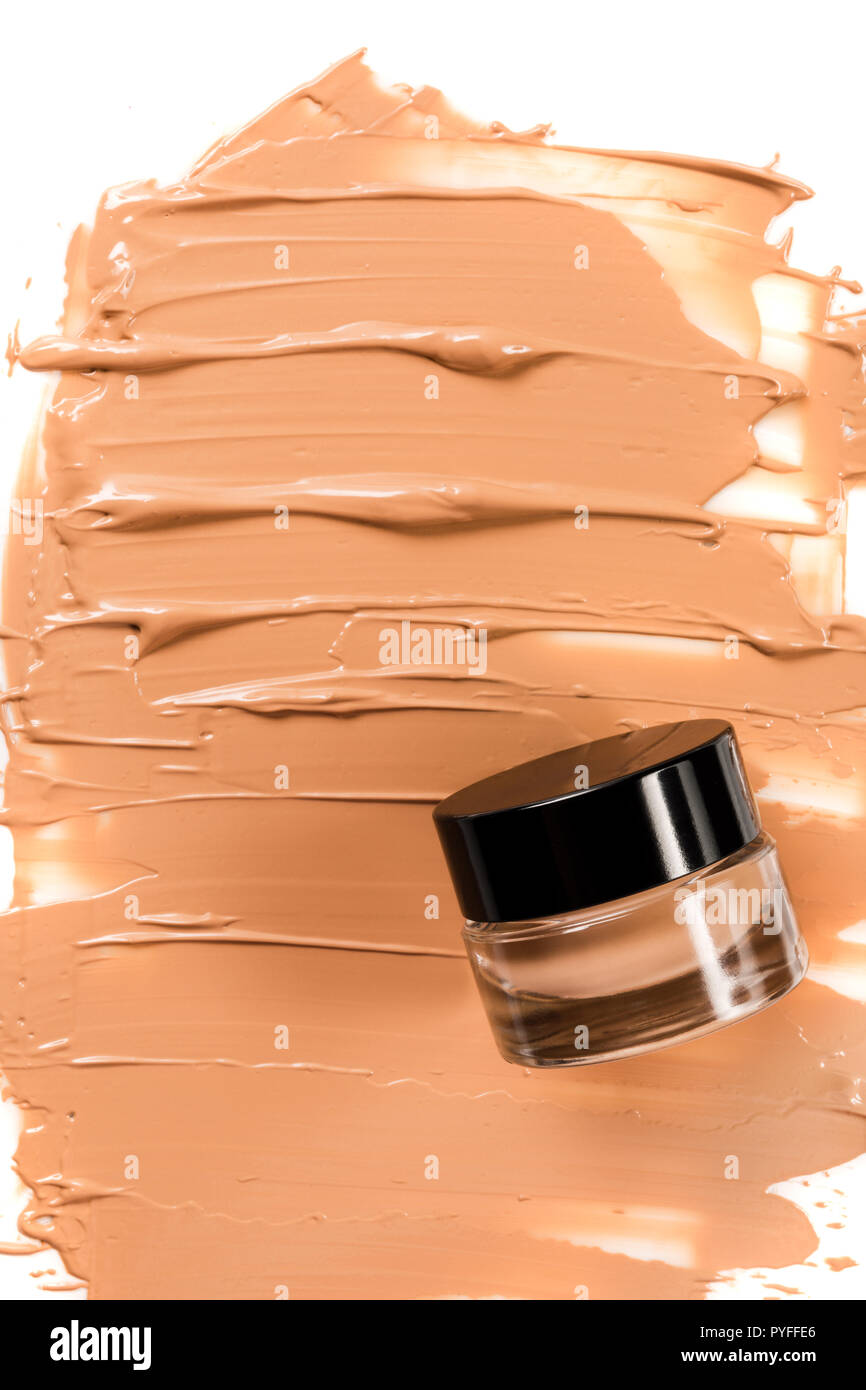 A glass jar of foundation for a face with a sample of the product