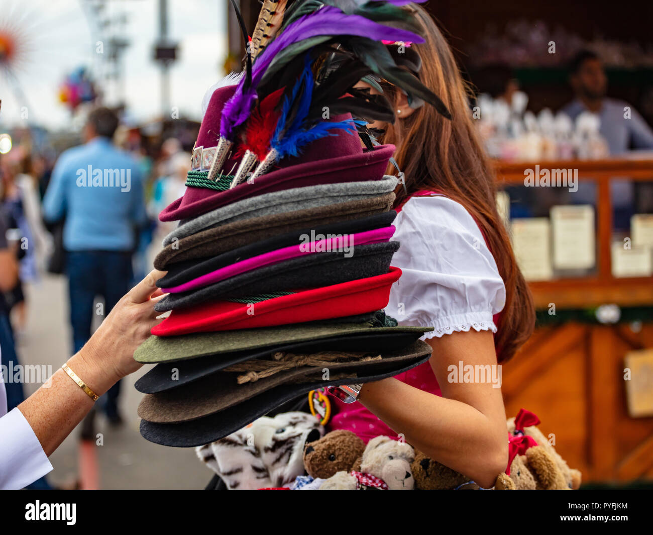 Young lady in tyrolean costume holding a stack of traditional hats, Oktoberfest, Munich, Bavaria Stock Photo