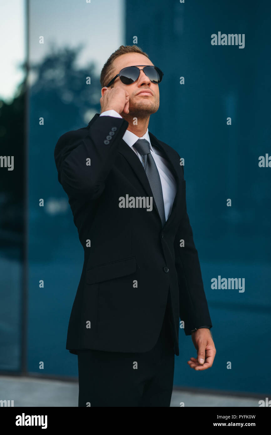 Male bodyguard talking by earpiece outdoors, security communication