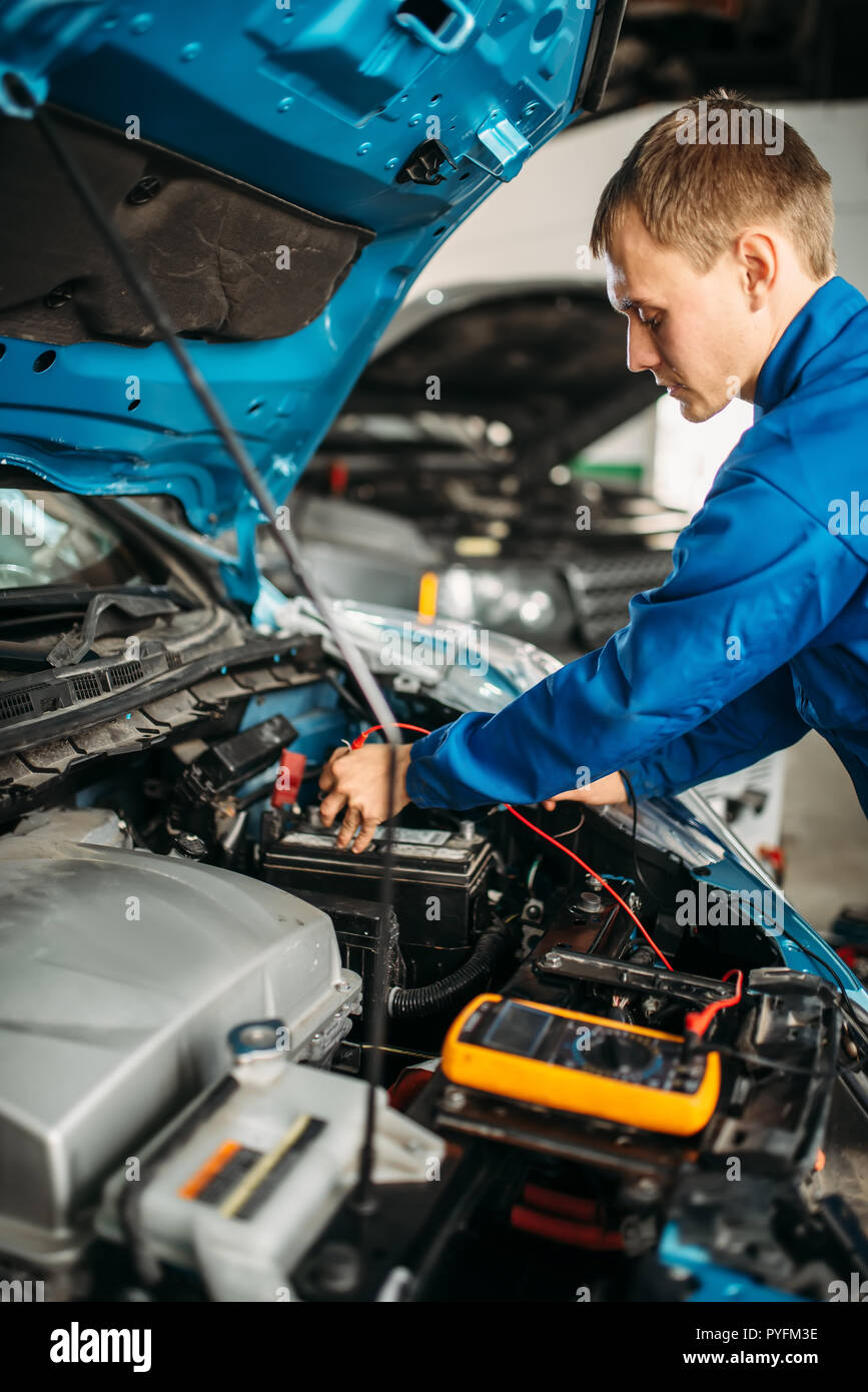 Car electrician with multimeter checks the battery level. Auto-service, vehicle wiring diagnostic Stock Photo