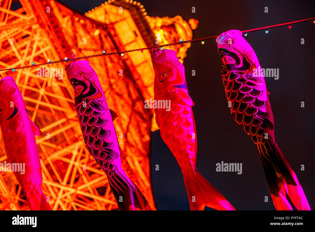 Tokyo, Japan - April 23, 2017: Koinobori a pink carp-shaped wind socks, traditionally flown in Japan to celebrate Children's Day. Blurred Tokyo Tower by night on background. Horizontal shot. Stock Photo