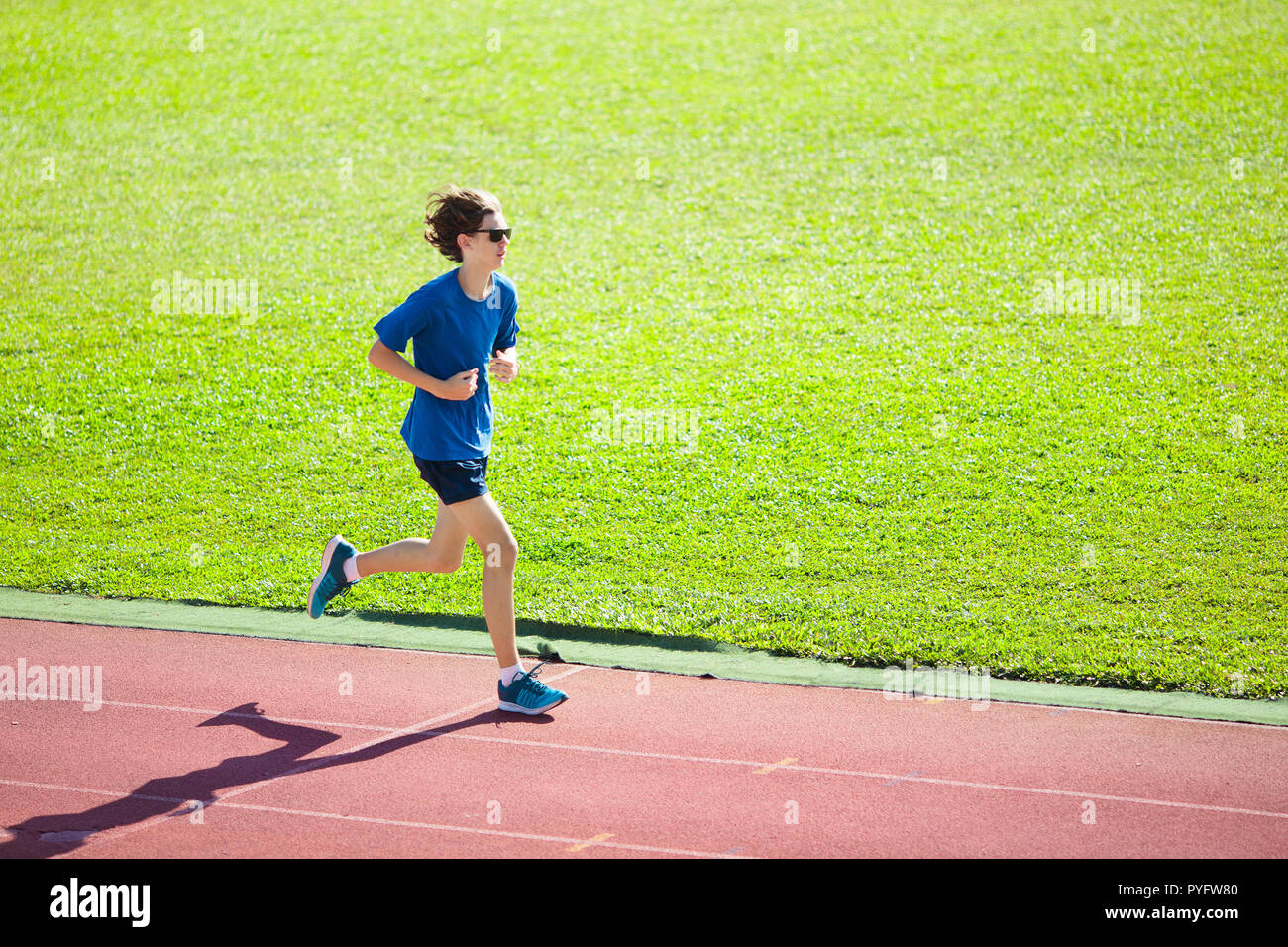 Boy running on outdoor stadium race track. Teenager sprinting during athletics training. Teenage kid jogging. Healthy sport for school kids. Young man Stock Photo