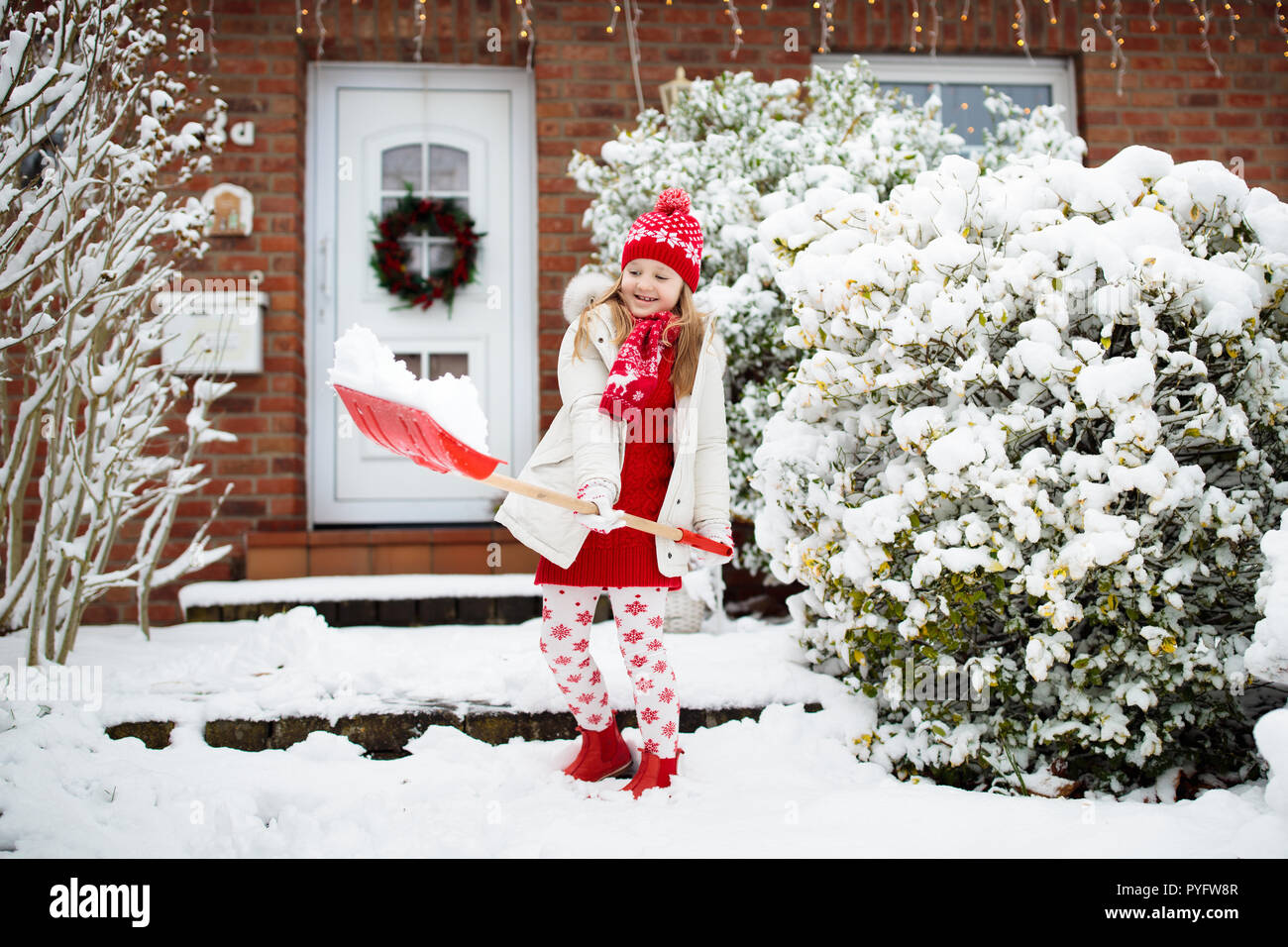 Child shoveling snow. Little girl with spade clearing driveway after winter snowstorm. Kids clear path to house door after Christmas blizzard. Snowfal Stock Photo