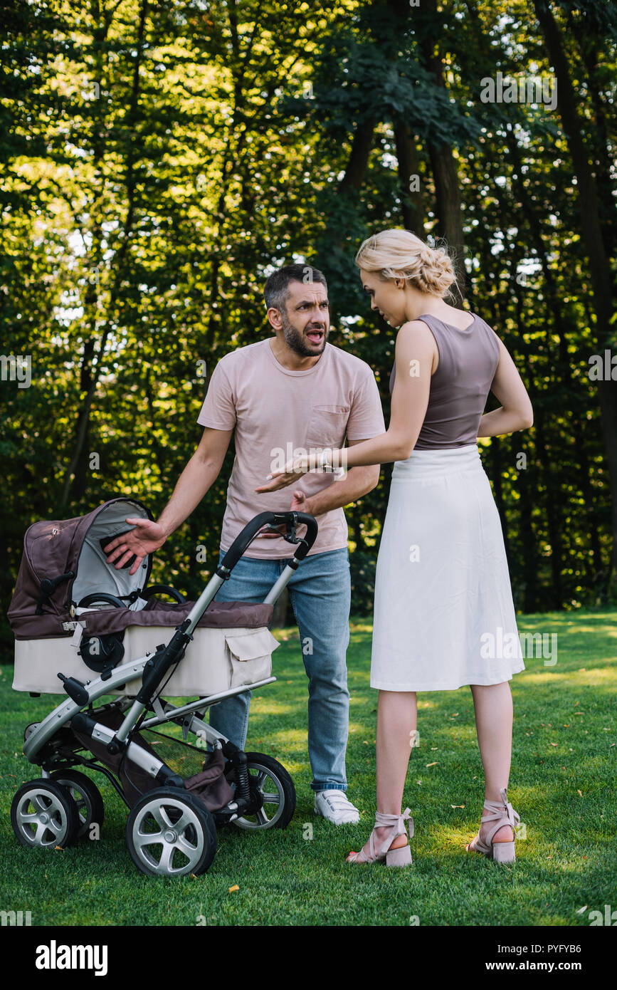 angry parents quarreling near baby carriage in park Stock Photo