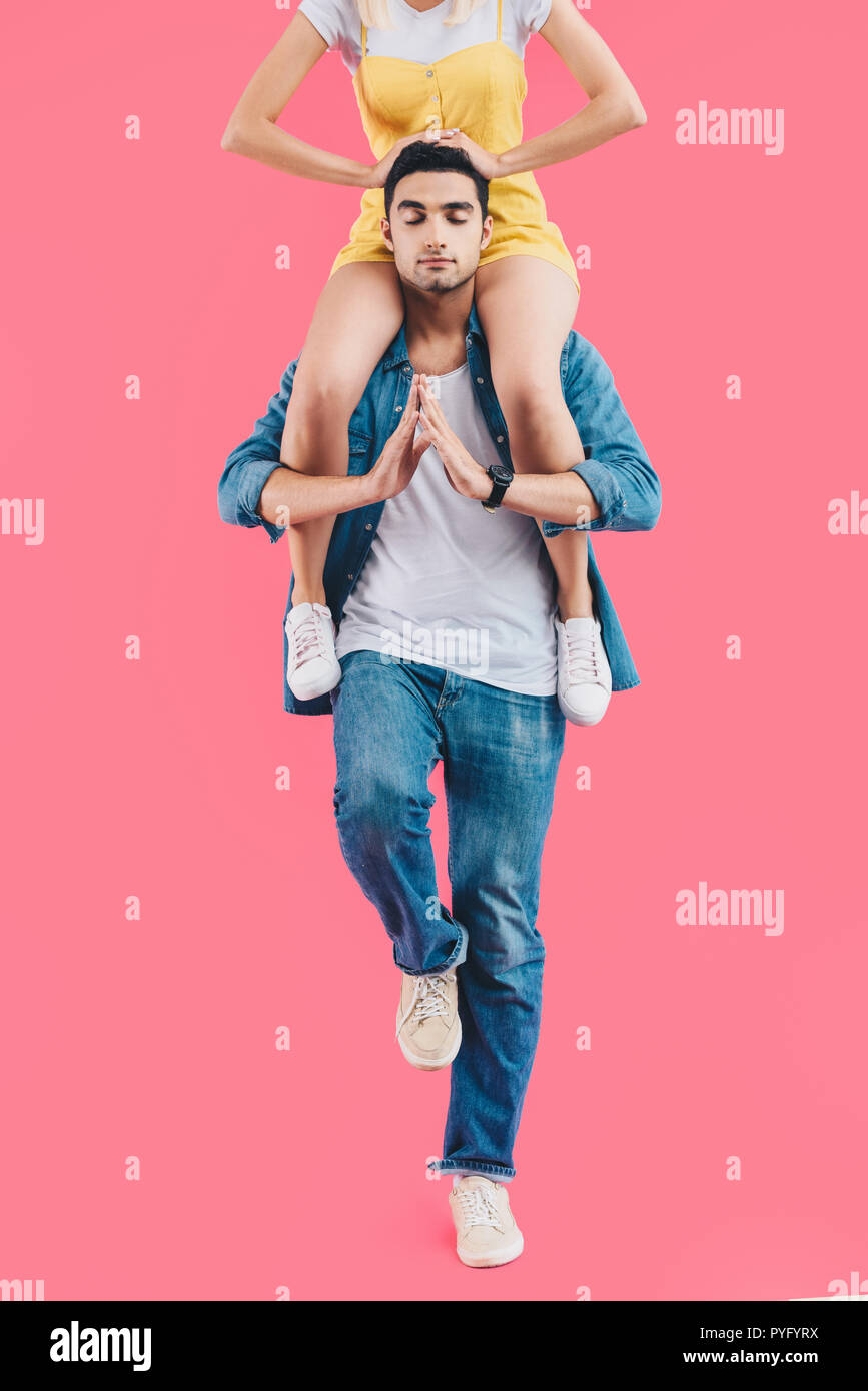 cropped image of woman sitting on shoulders of boyfriend while he meditating with closed eyes isolated on pink Stock Photo