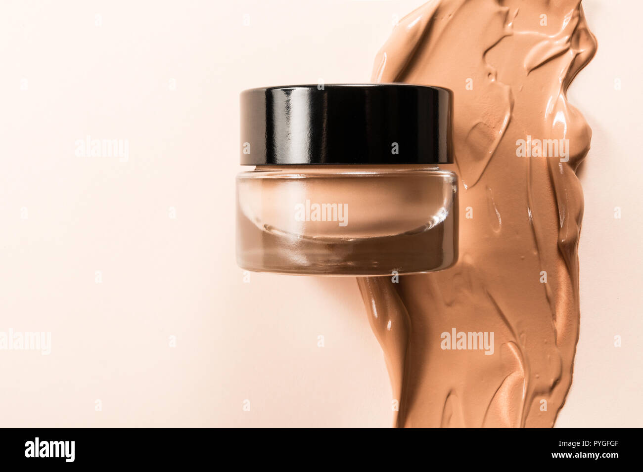 A glass jar of foundation for a face with a sample of the product itself. Stock Photo