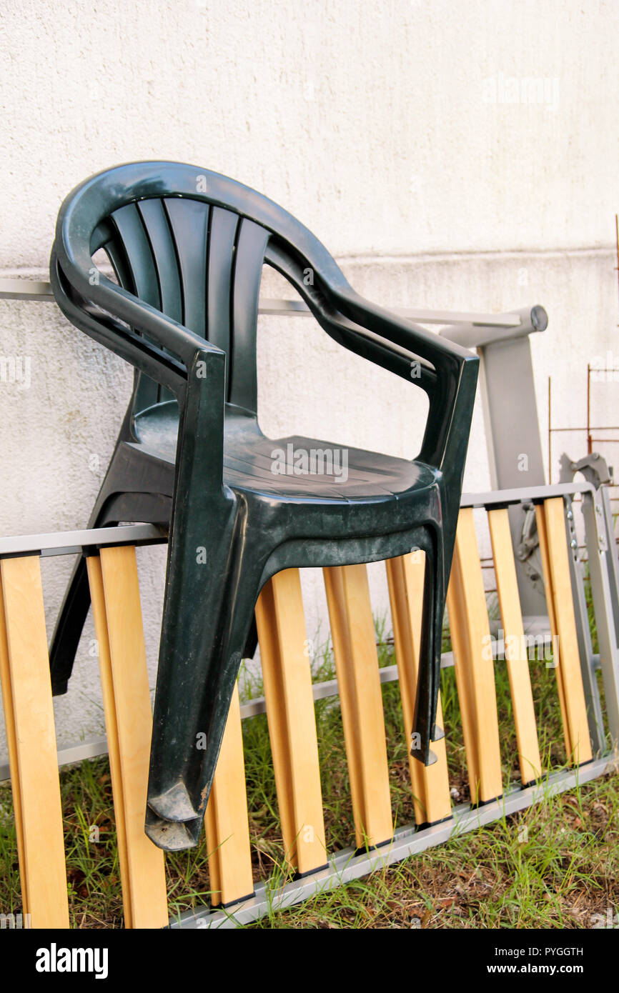 Green plastic garden chairs thrown away and left on a ladder by the