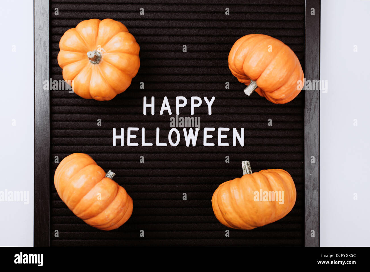 Happy Halloween words on black letter textured board. It is in frame with small yellow pumpkins. Flat lay style. Stock Photo