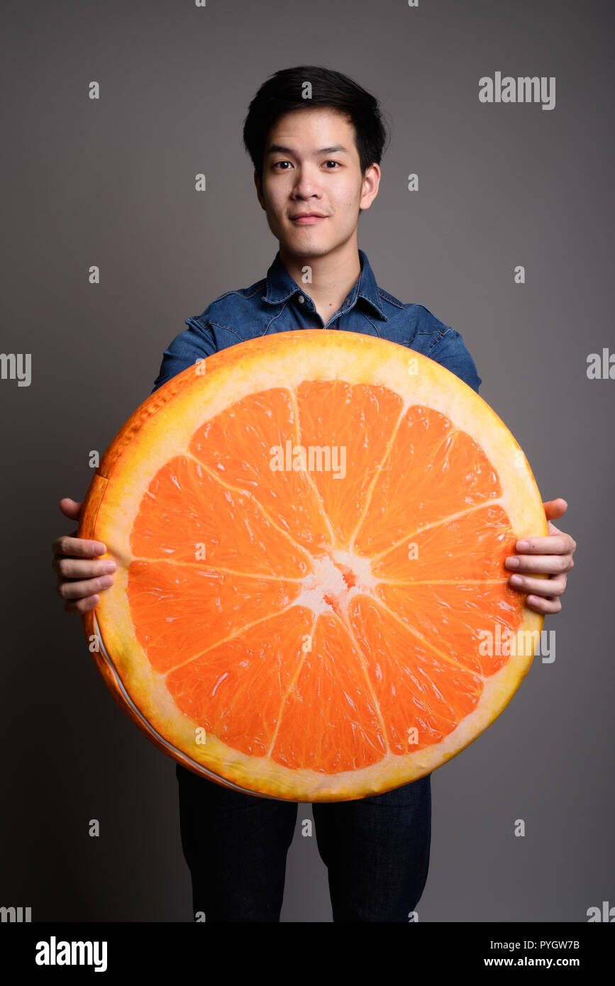 Young handsome Asian man holding orange fruit pillow Stock Photo