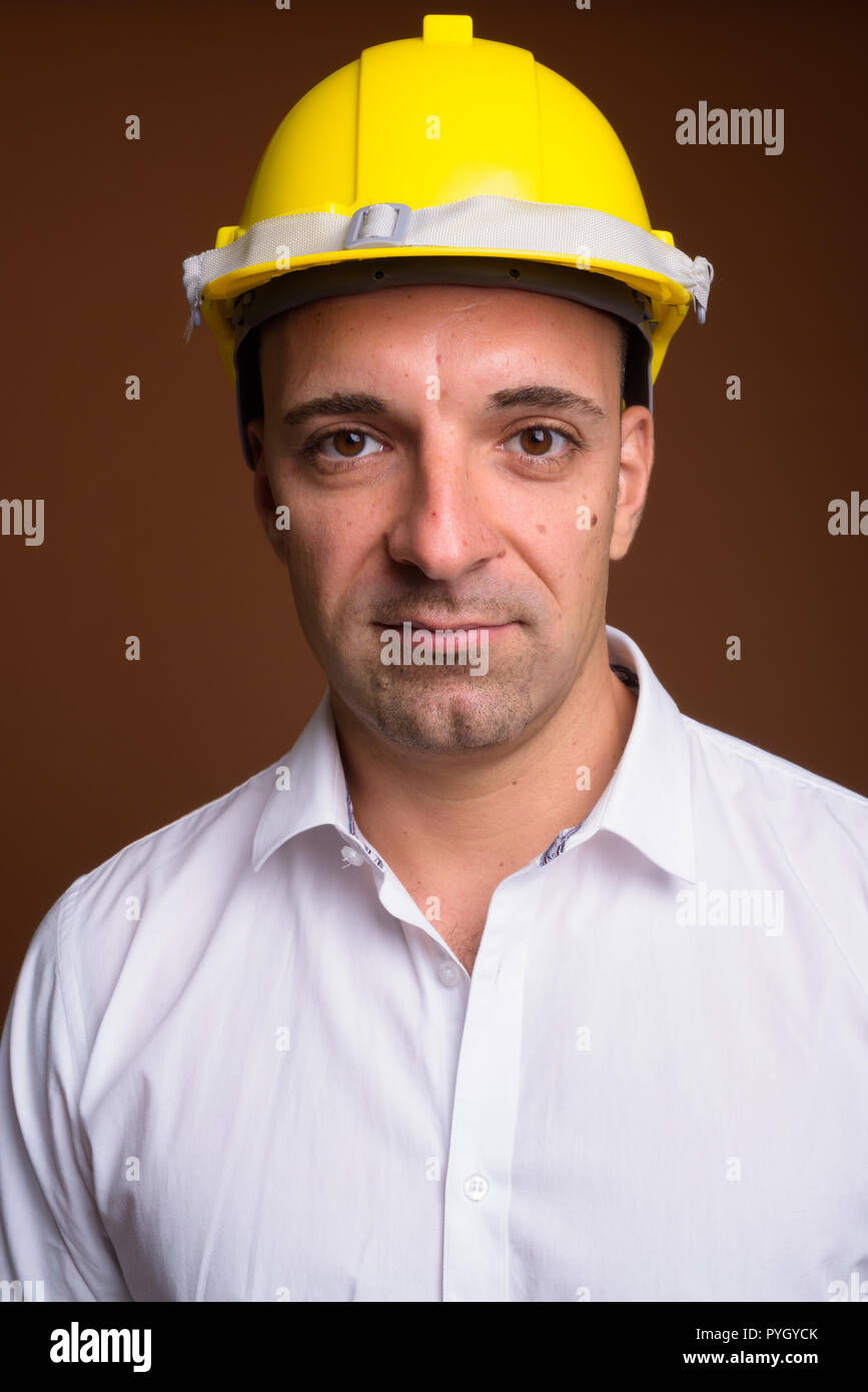 Portrait of businessman wearing hardhat against brown background Stock Photo