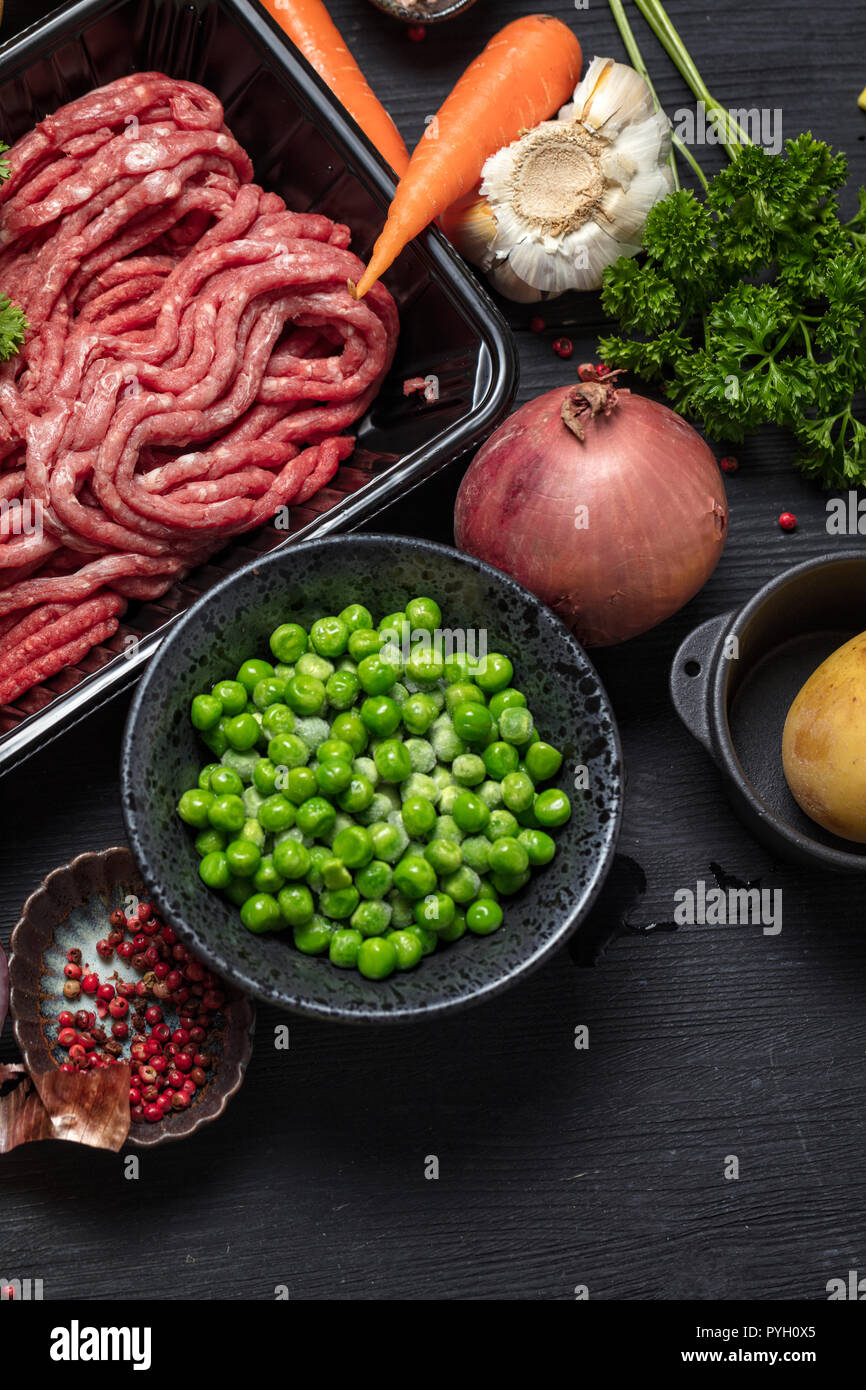Raw minced meat in container surrounded by ingredients for shepherds
