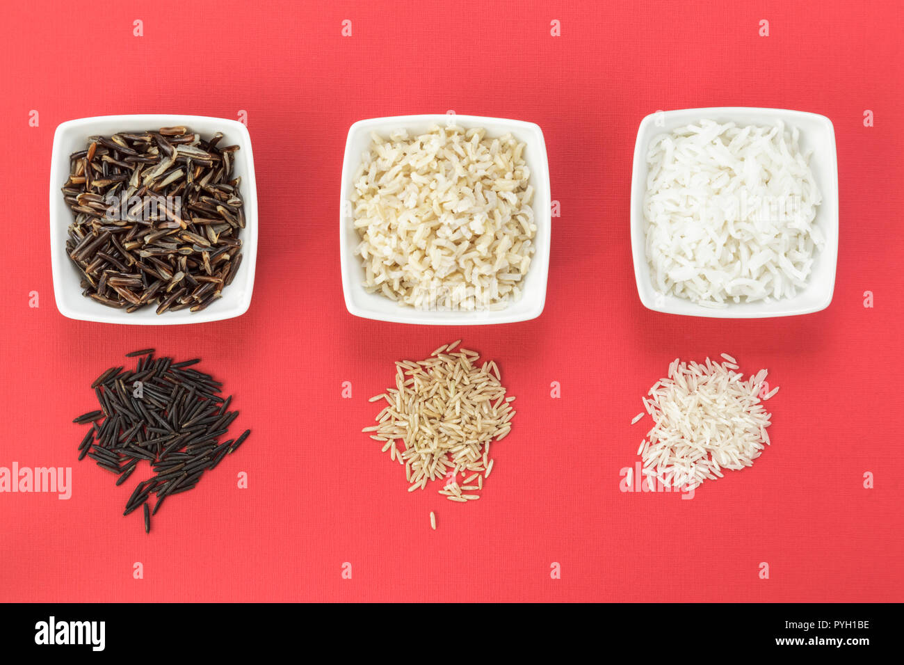 Cooked and uncooked wild, brown and white rice on red background Stock Photo