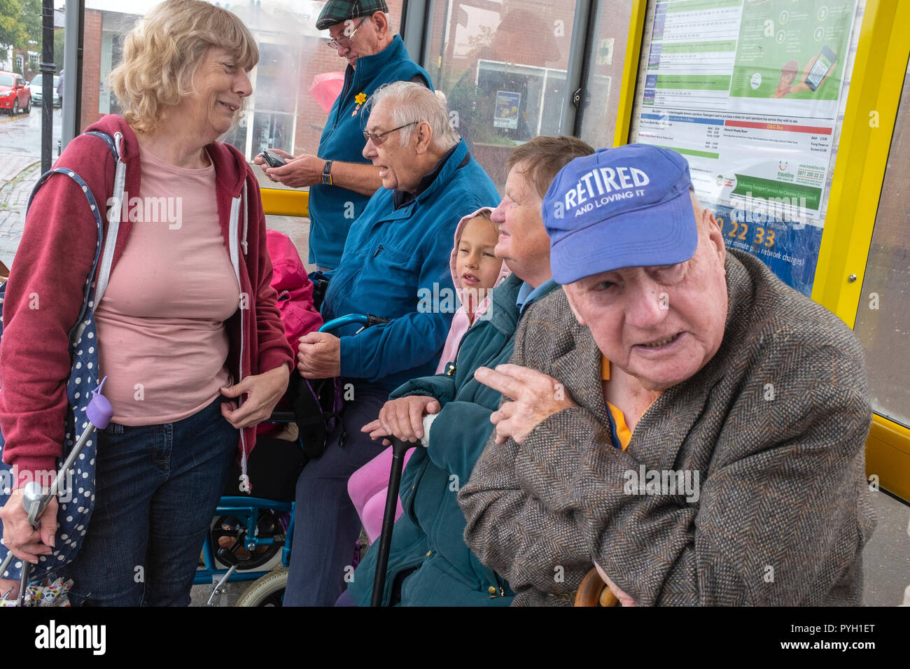Pensioner wearing cap saying Retired and loving it at a bus station in Sandbach Cheshire UK Stock Photo