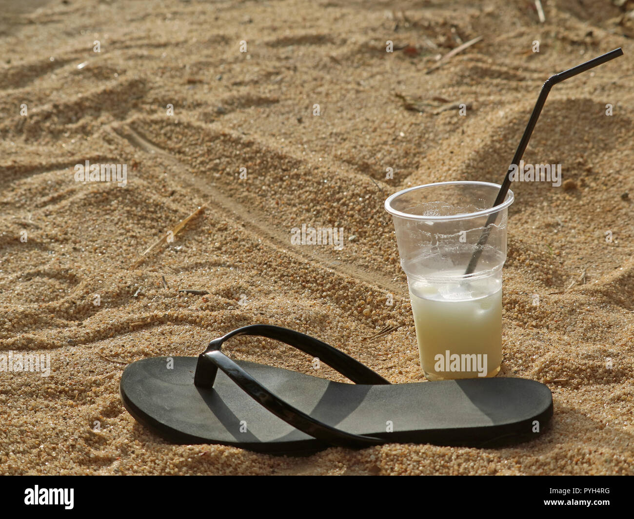 single black beach slipper and cocktail in plastic cup with drinking straw on beach in holidays Stock Photo