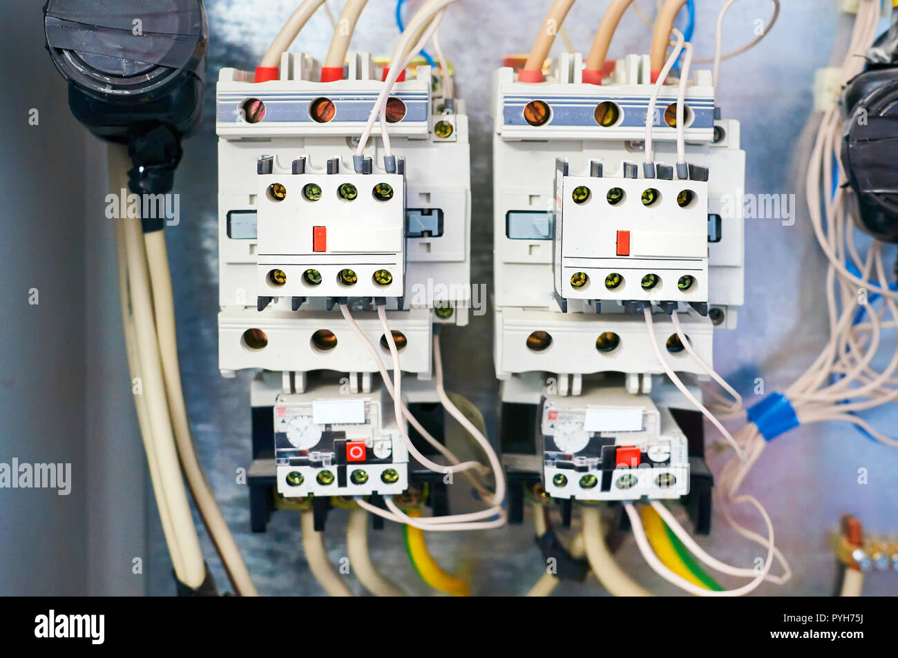 Two electric relays are connected by wires to the metal background. Stock Photo