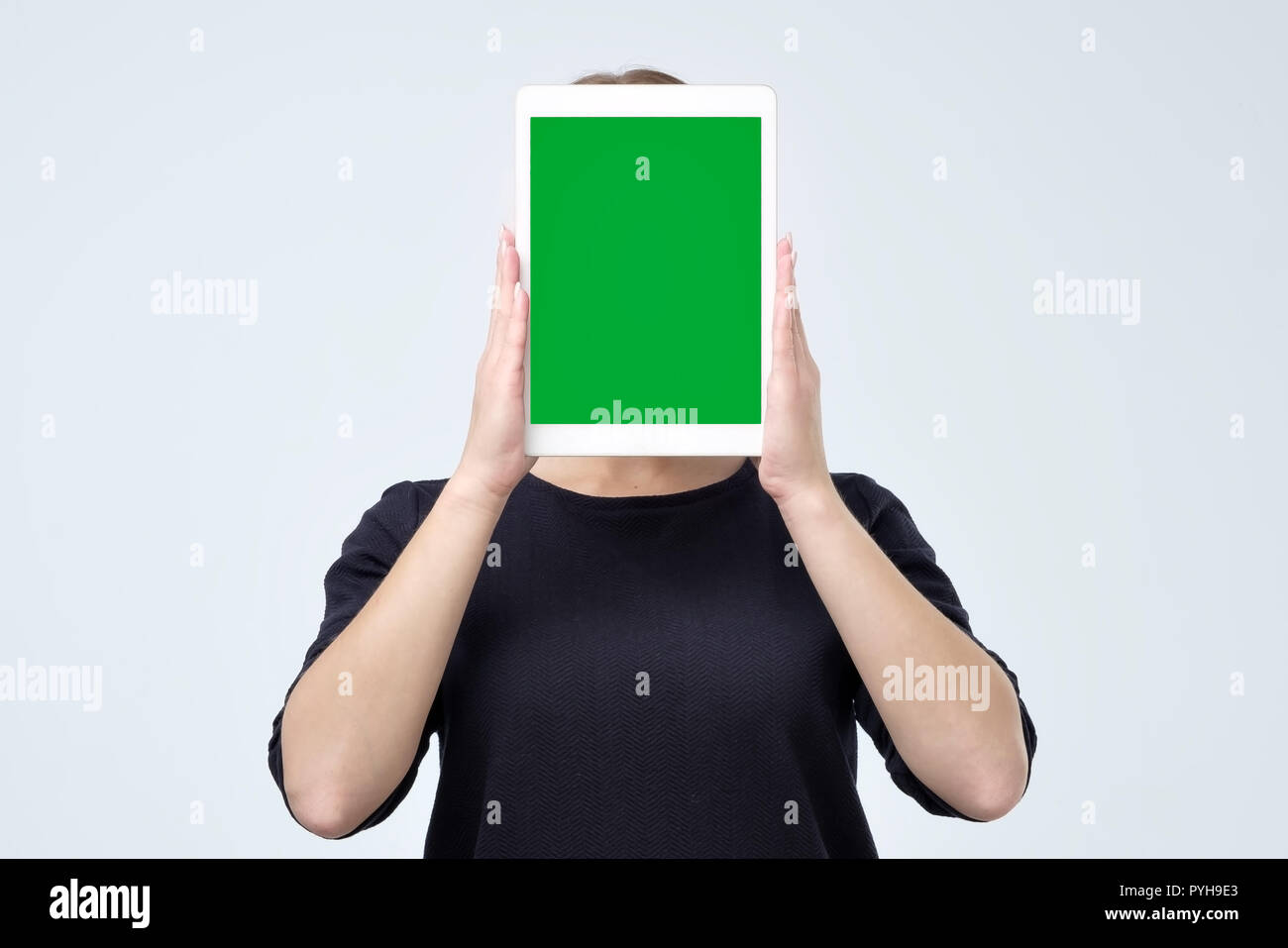 Young woman holding up a blank tablet in front of her face with the screen with copy space facing the viewer Stock Photo