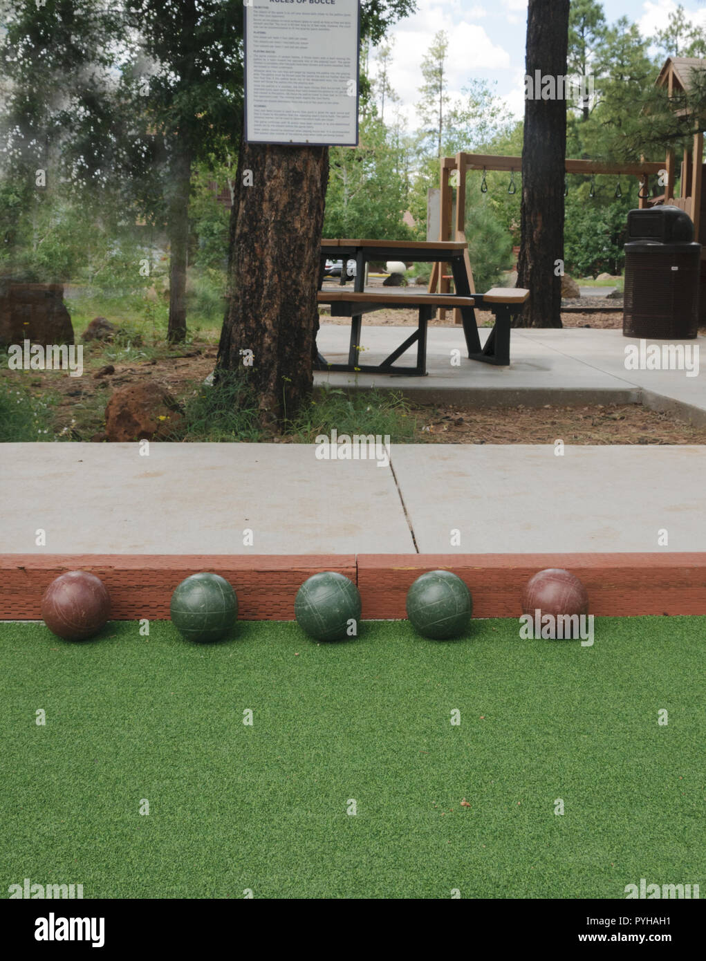 5 bocce balls on edge of bocce court, three green balls and 2 red balls