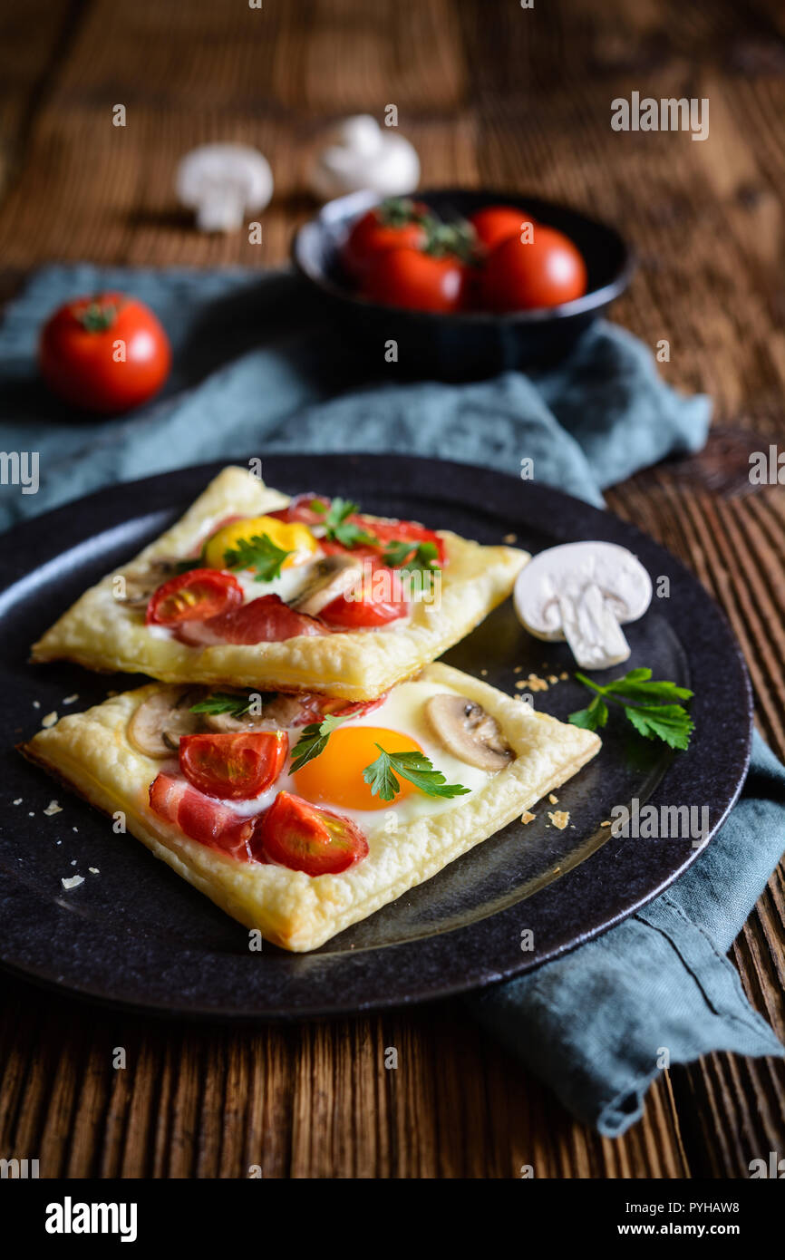 Savory puff pastry pies with egg, bacon, mushrooms and tomato Stock