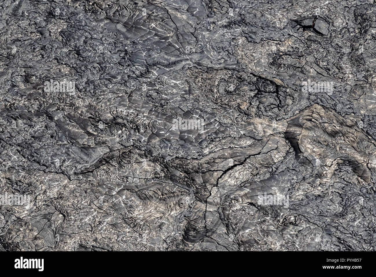 Aerial view of Puu Ooo Volcanic lava field. The pahoehoe lava's surface is swirled and wrinkled, reflecting silver. Giant cracks from cooling. Stock Photo