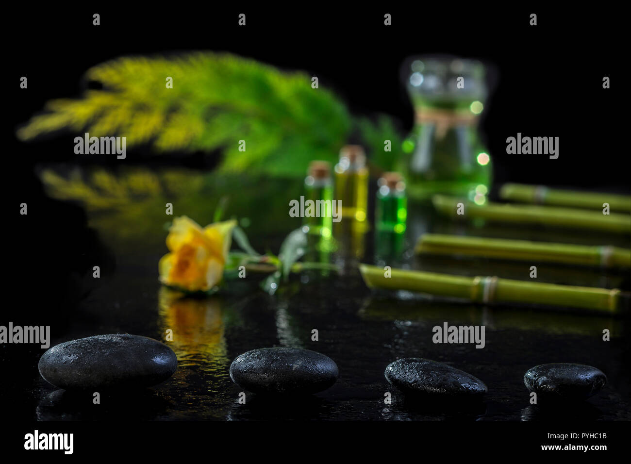 Beautiful spa composition with zen basalt stones and bamboo essential oil plants and flowers on black Stock Photo