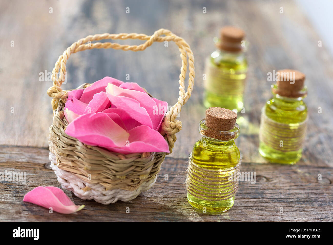 Rustic wicker basket with pink rose hip flowers and bottles of essential roses oil on wooden background Stock Photo
