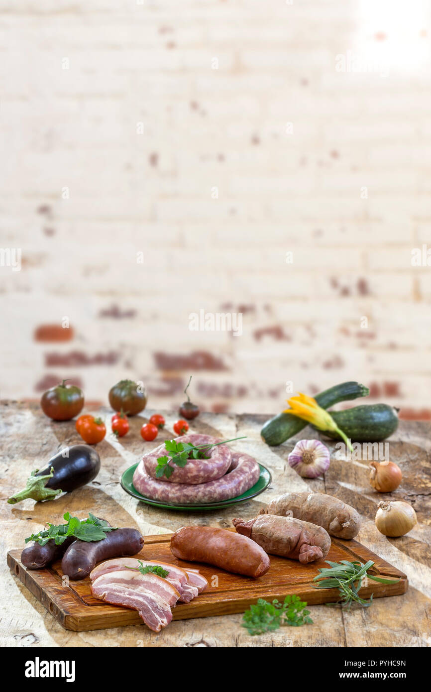 Selection of French Raw sausage with arugula leaves in a wooden board,vegetable on the table on old white cracked red brick wall background. Stock Photo