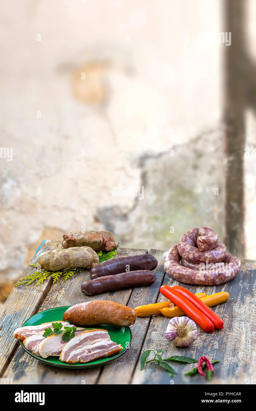 Selection of French Raw sausage with arugula leaves in a wooden board,vegetable on the table on old white cracked wall background. Stock Photo