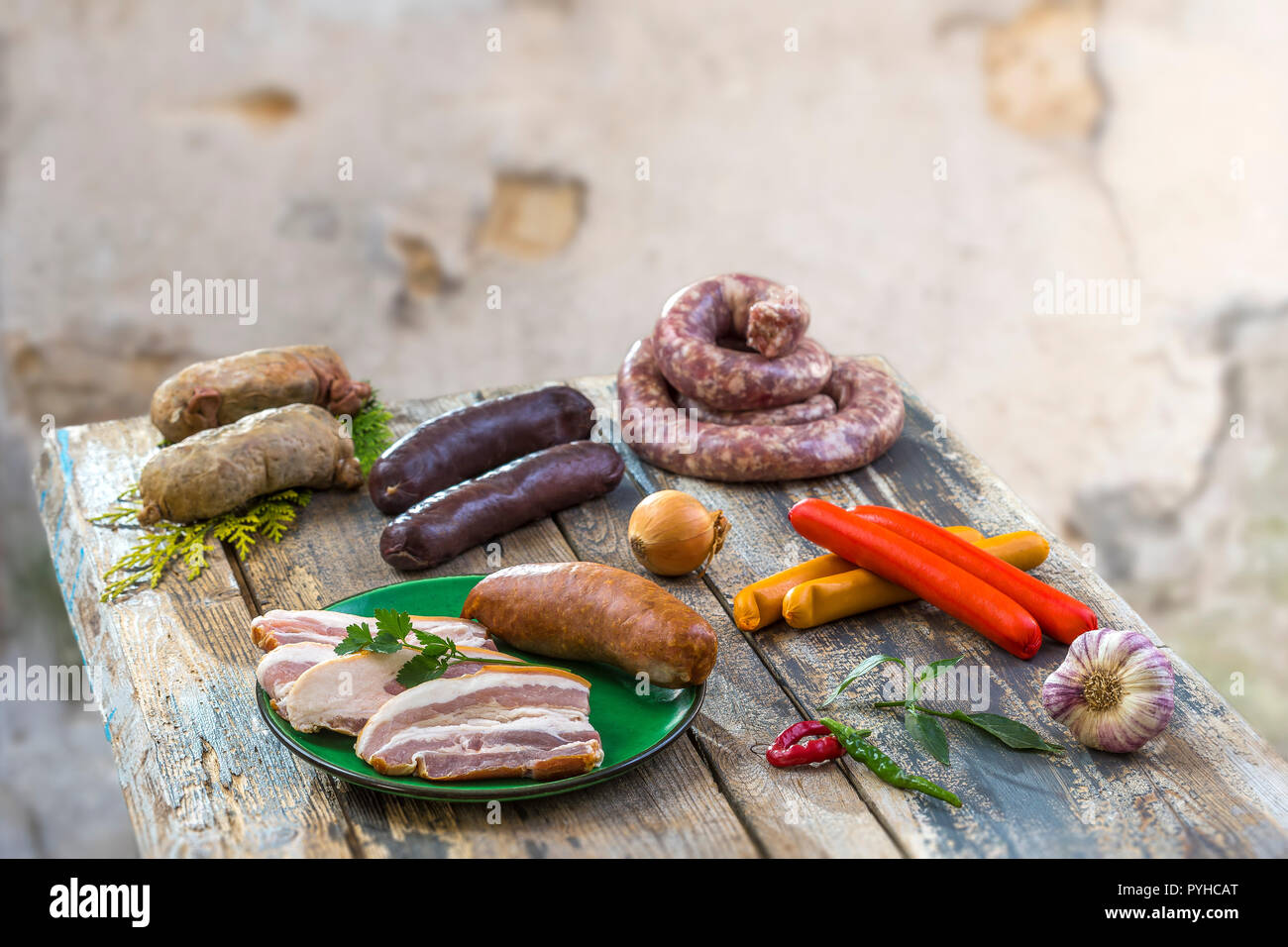 Selection of French Raw sausage with arugula leaves in a wooden board,vegetable on the table on old white cracked wall background. Stock Photo