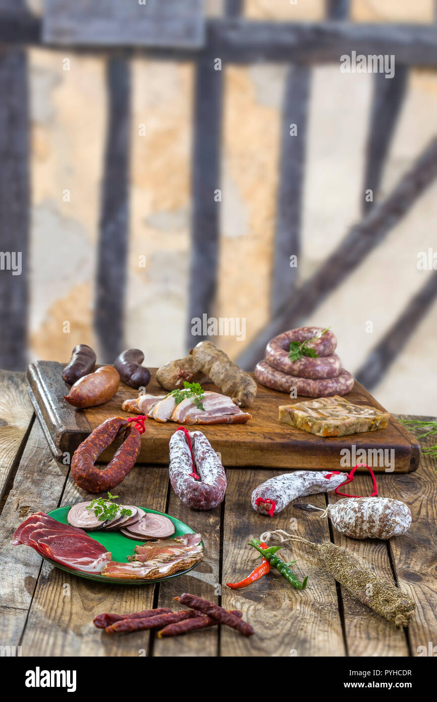 Selection of French Raw charcuterie board, with arugula leaves and dry sausage over old brown timbered wall background. Stock Photo
