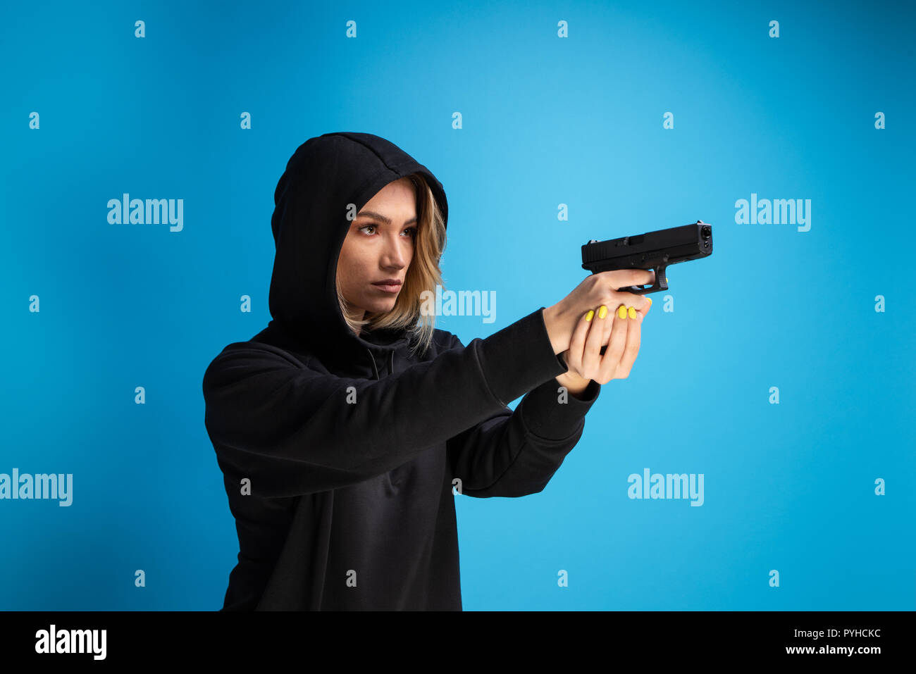 Hooded girl holding a gun pointed to the right side. Criminal face adult gangster Stock Photo