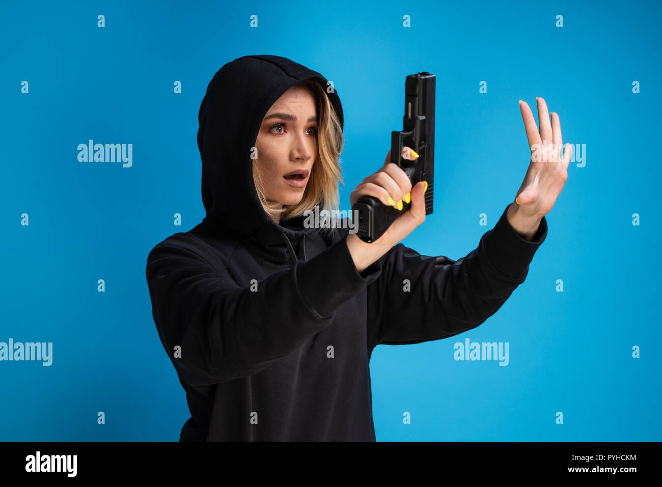 Hooded young girl presenting gun while surrendering. Airsoft game loser Stock Photo