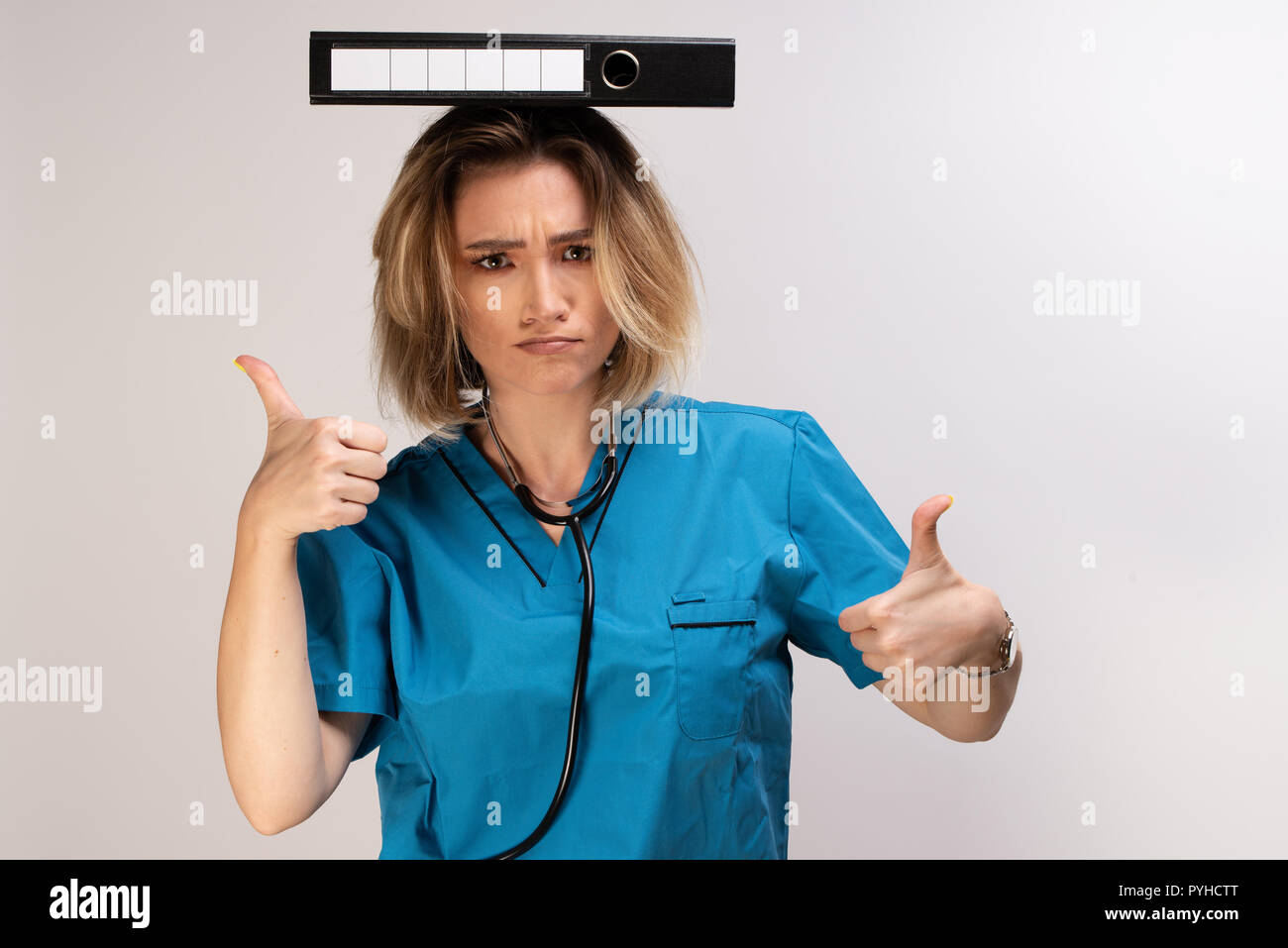 Crazy female doctor balancing documents on her head displaying thumbs up. Positive doctor attitude Stock Photo