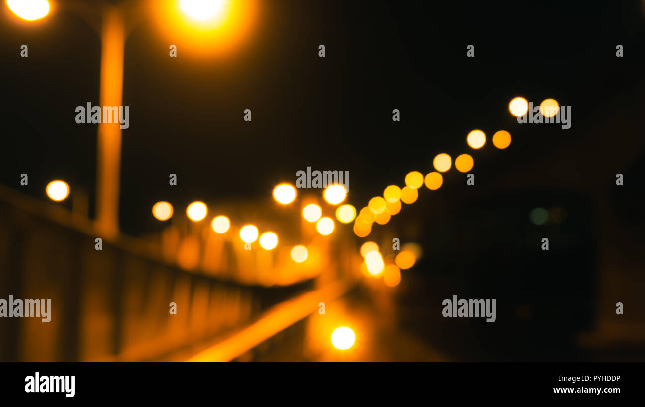 Blurred bridge, road, and electric pole with yellow bokeh in the night. Night life concept. Gold, white, and orange bokeh of lights in street. Lonely  Stock Photo