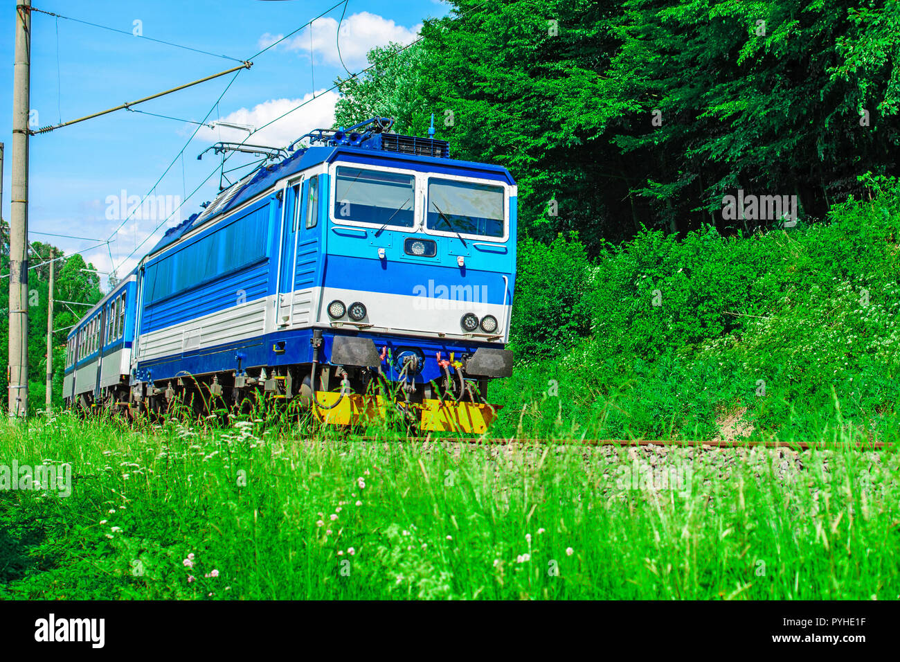 A blue electric locomotive passing the Czech countryside. A train running through the green valley. Rail transport in the Czech Republic Stock Photo