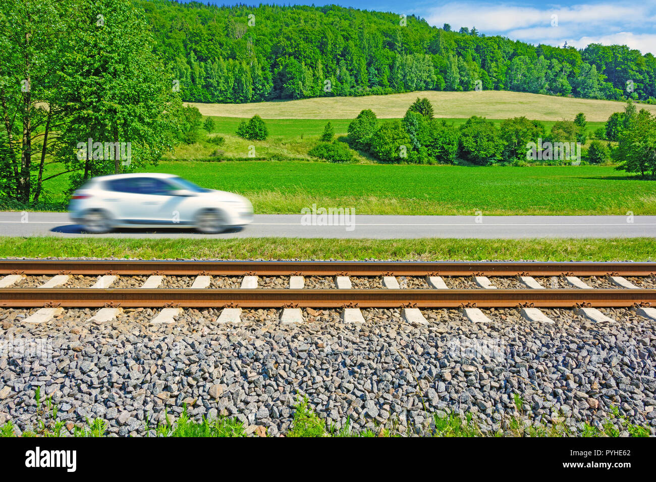 A fast moving car along the road goes alongside the railway tracks. Tracks running next to the A fast moving car along the road goes alongside the railway tracks. Tracks running next to the