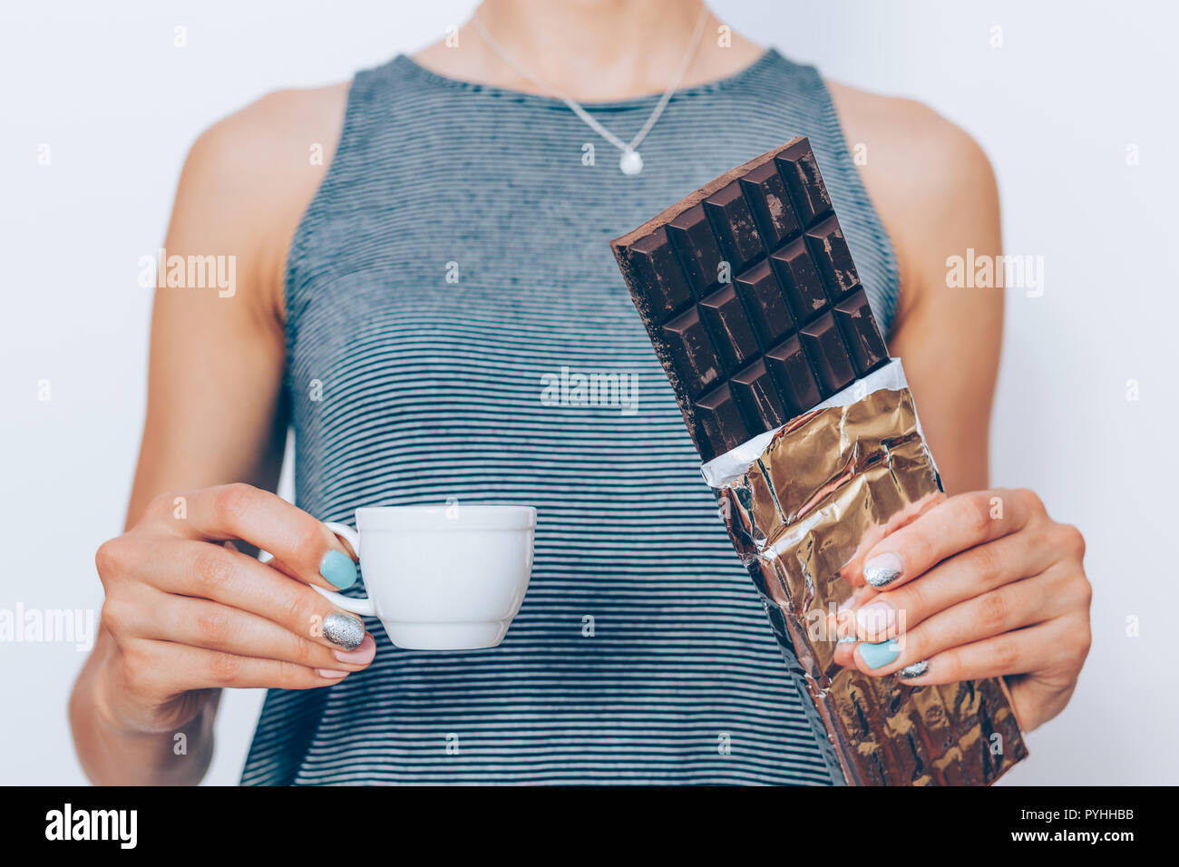 Cropped image of slender female with chocolate bar and coffee. Woman's hands holding unwrapped cocoa dessert in foil and cup of fresh espresso, close- Stock Photo