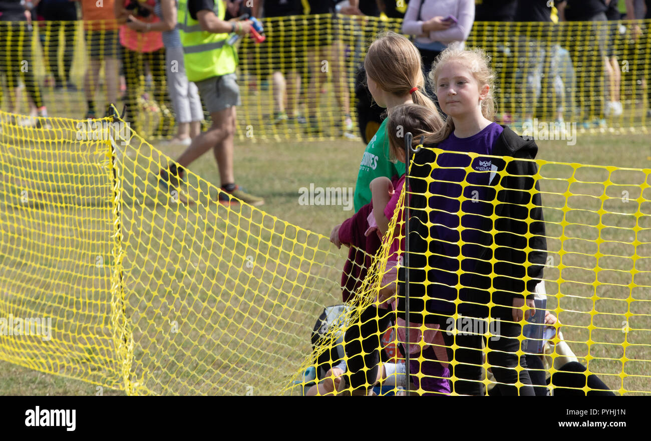 Some young girls behind a yellow plastic mesh fence waiting for an obstacle course race to pass Stock Photo