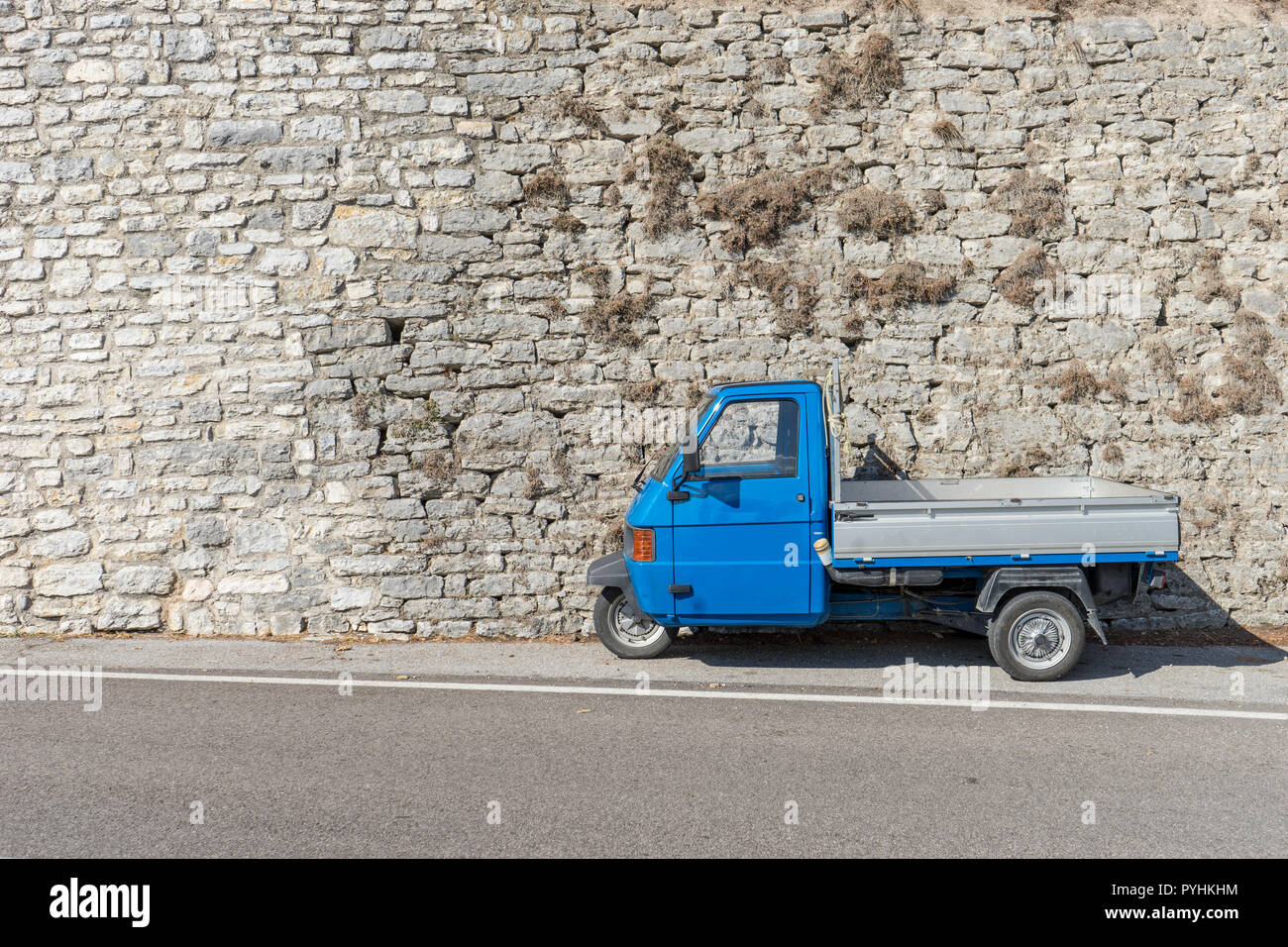 Blue, small transport vehicle in front of a bright stone wall Stock Photo