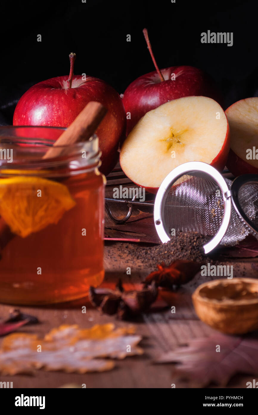Dark wooden table with 2 glasses of tea with fall, autumn decoration and dark, black background. Colourful leaves, lemon, cinnamon, walnuts, apples, t Stock Photo