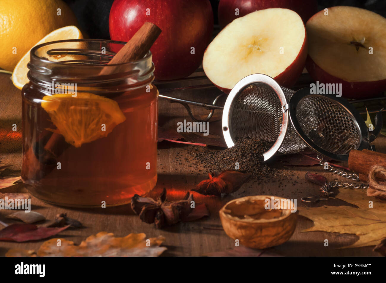 Dark wooden table with 2 glasses of tea with fall, autumn decoration and dark, black background. Colourful leaves, lemon, cinnamon, walnuts, apples, t Stock Photo