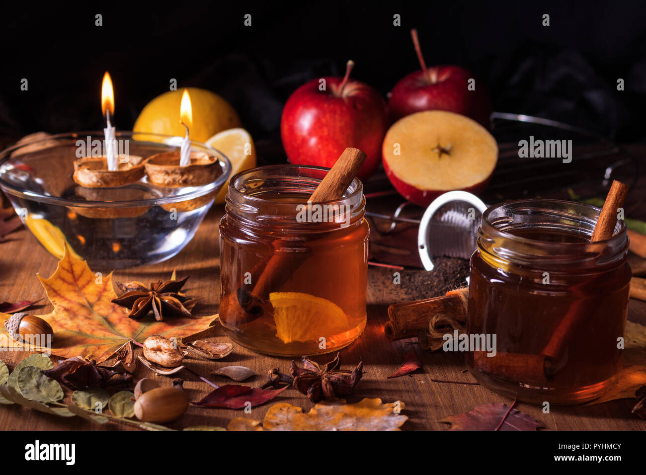 Dark wooden table with 2 glasses of tea with fall, autumn decoration and dark, black background. Colourful leaves, lemon, cinnamon, walnuts, apples, t Stock Photo