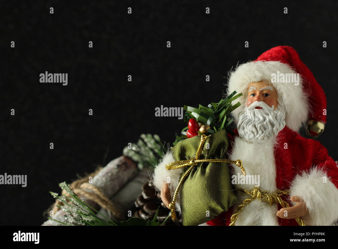 Santa Claus holding a sack of presents close up standing next to tied bundle of logs on a black background with writing space Stock Photo