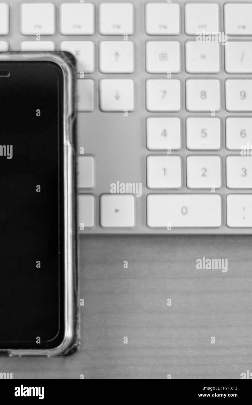 monochrome close up of a smartphone lying on a white keyboard, dektop Stock Photo