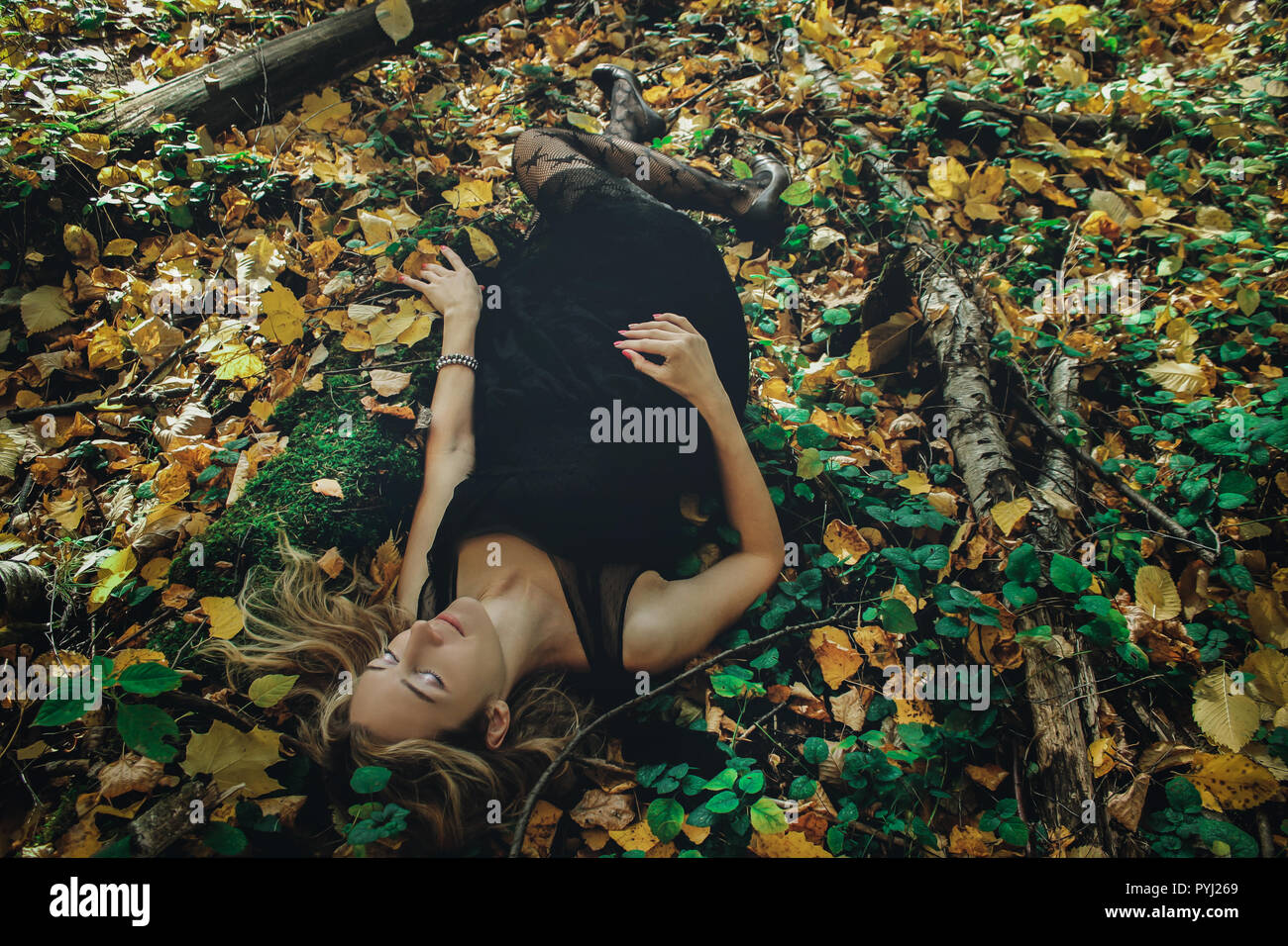 A young kind witch in a black dress with a black mask in a mystical forest in various poses. Art processing Stock Photo