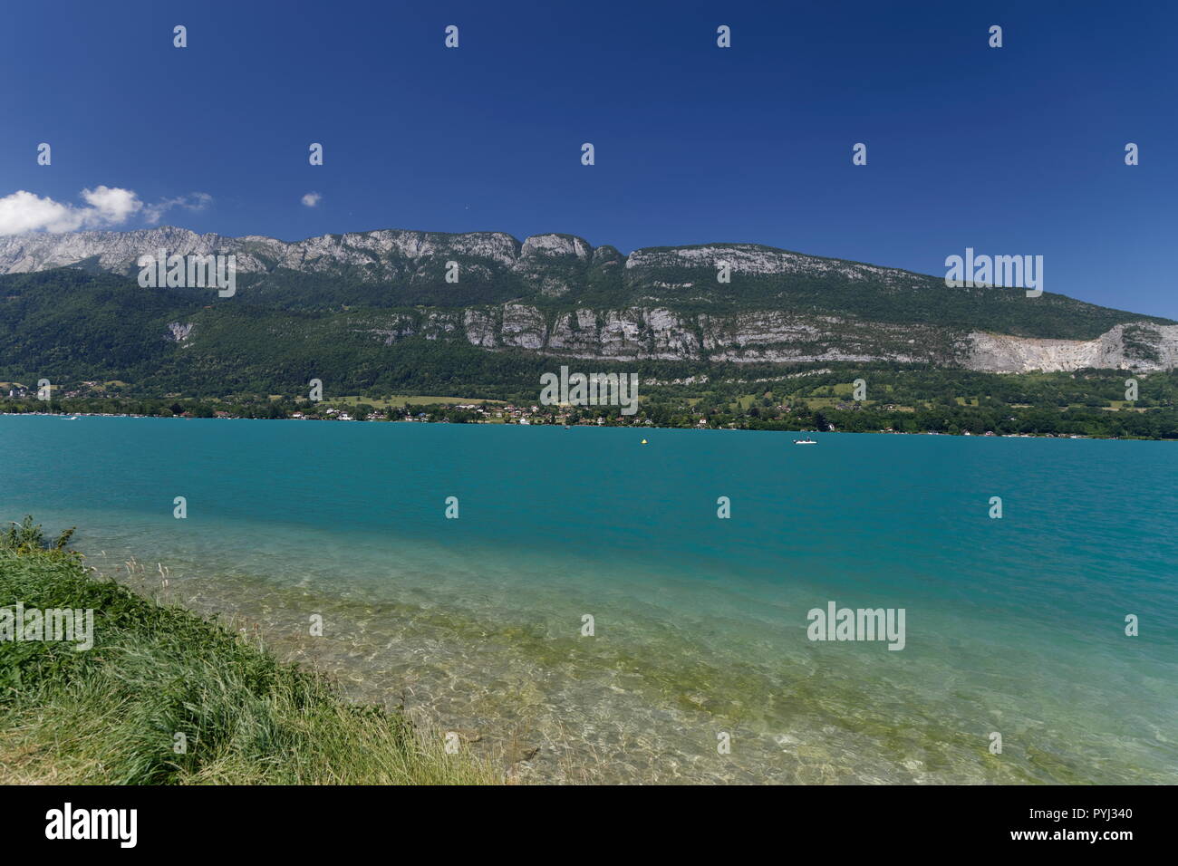 Beautiful clear turqoise water of Lake Annecy with boats and distant mountains France Stock Photo