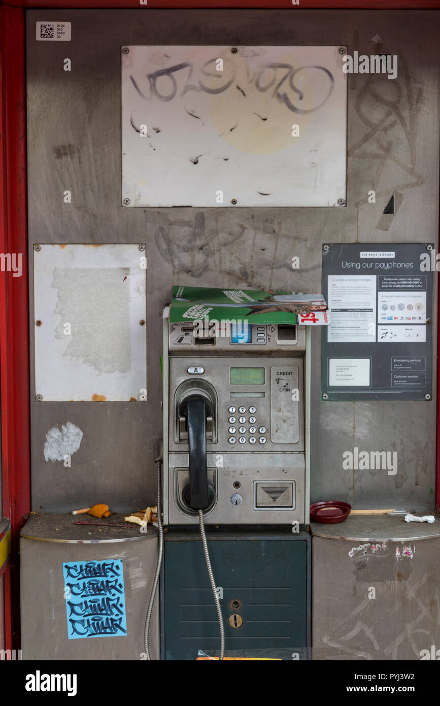 a dirty and vandalised filthy unclean public telephone box in central London with graffiti on the sides and walls. Stock Photo