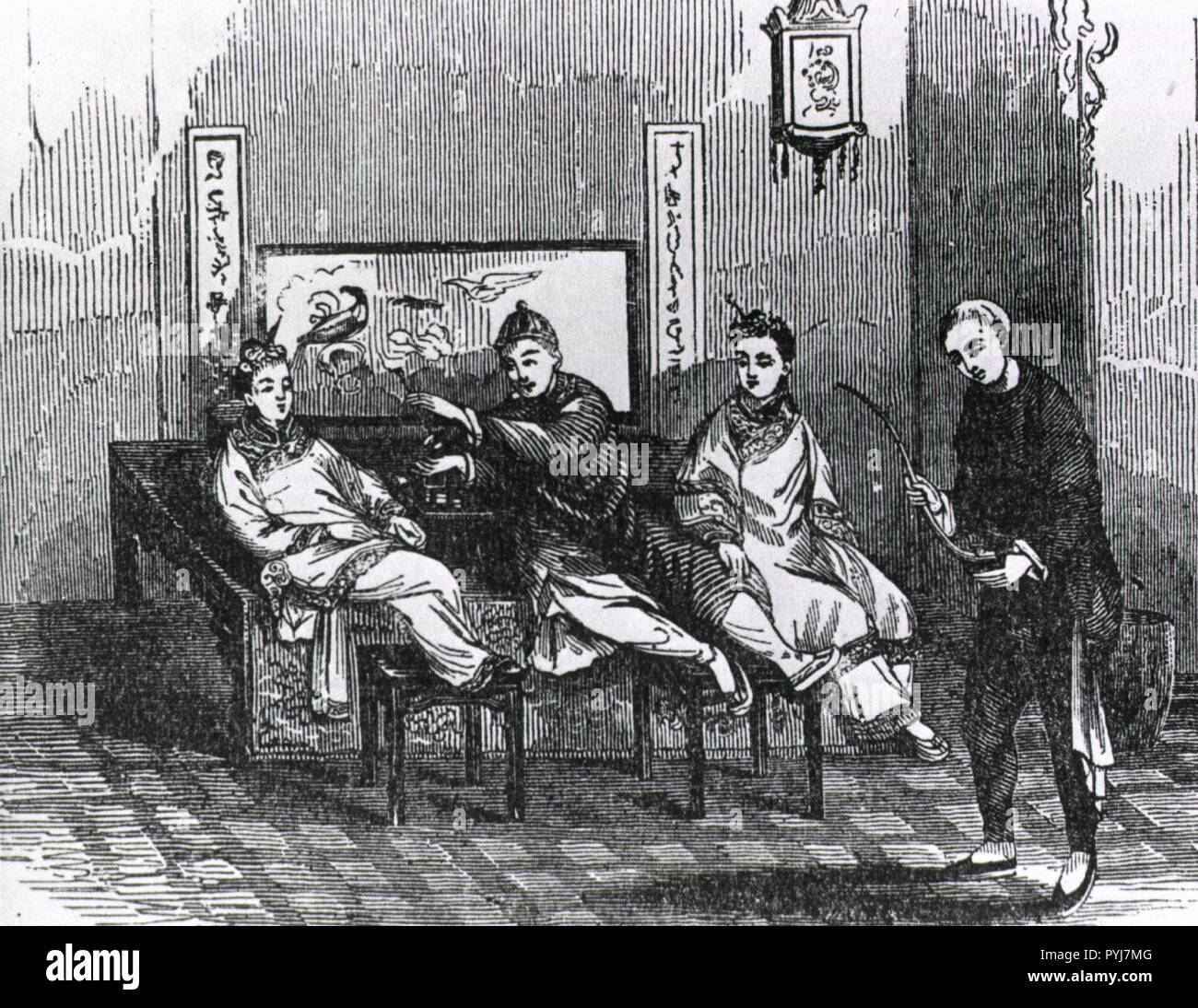 Interior view: two women and a man are sitting back on a raised platform, two of them are resting their feet on foot stools; the man appears to be passing a pipe to the woman on the left; another man has entered the room carrying a pipe. Stock Photo